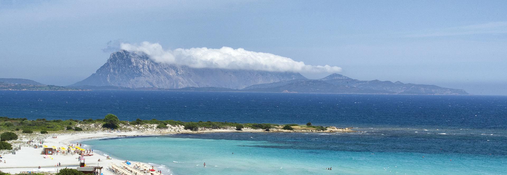 White ferry sails on blue sea with mountains in the background.